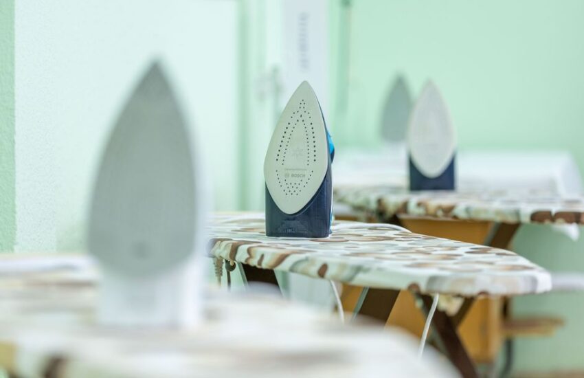 Close-up of modern irons placed on ironing boards with camouflage pattern covers in a bright indoor setting.