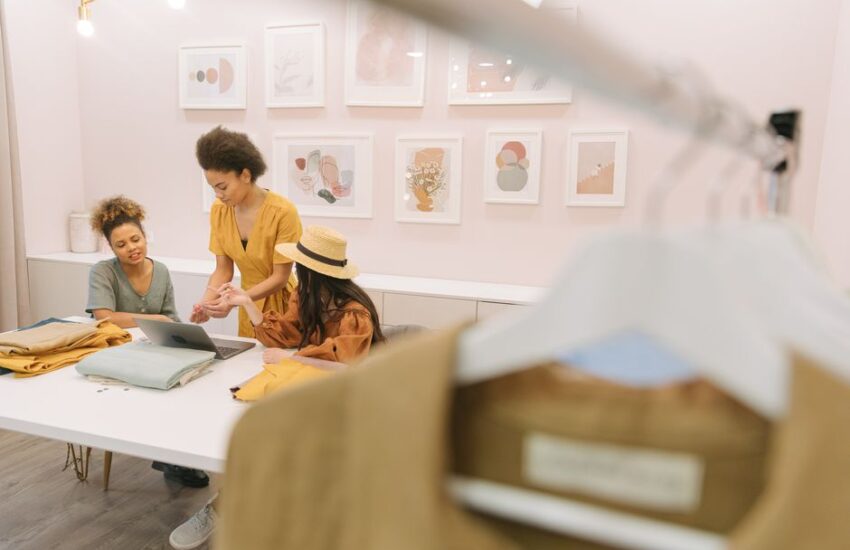 Three women engaged in brainstorming session with fabrics and laptop in a stylish fashion studio.