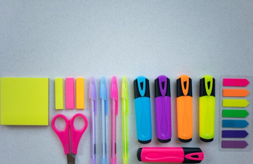 Flat lay of colorful school supplies including pens and highlighters on a white surface.
