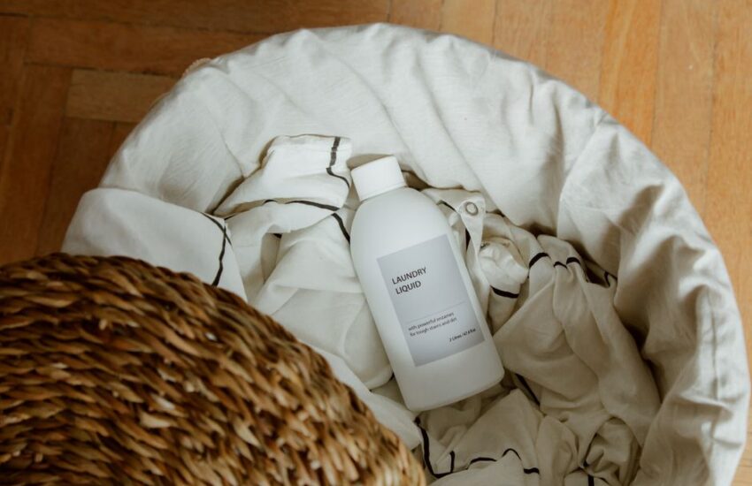 High angle view of laundry liquid in basket with white linens on wooden floor.