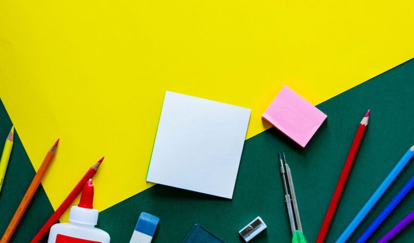 A vibrant flat lay of various school supplies on a yellow and green geometric background.