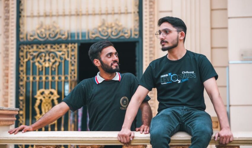 Two young men in casual outfits enjoying a moment on a decorative palace balcony.