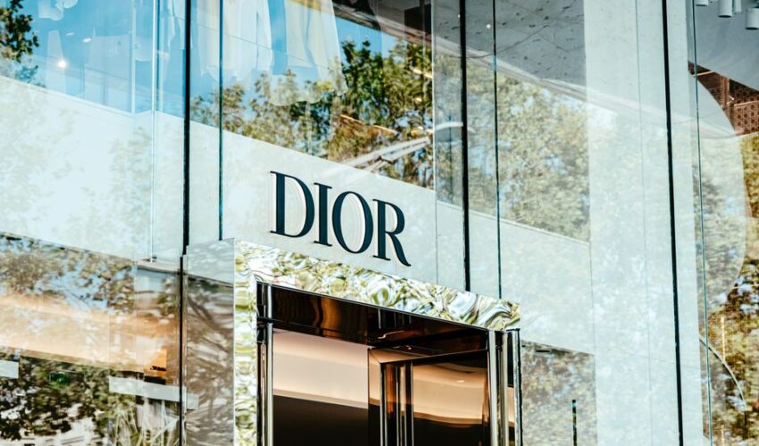 Exterior of a Dior store with glass facade reflecting trees and architecture.