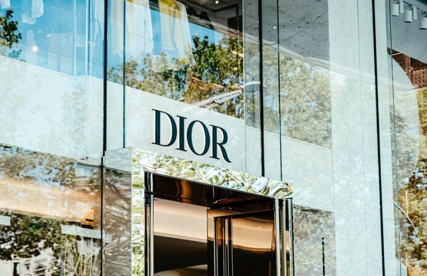 Exterior of a Dior store with glass facade reflecting trees and architecture.